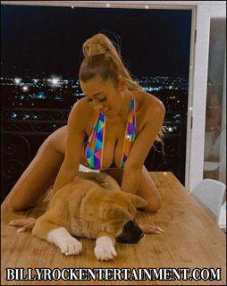Exotic dancer Maggie sitting on a table with a cute dog, wearing a vibrant swimsuit.